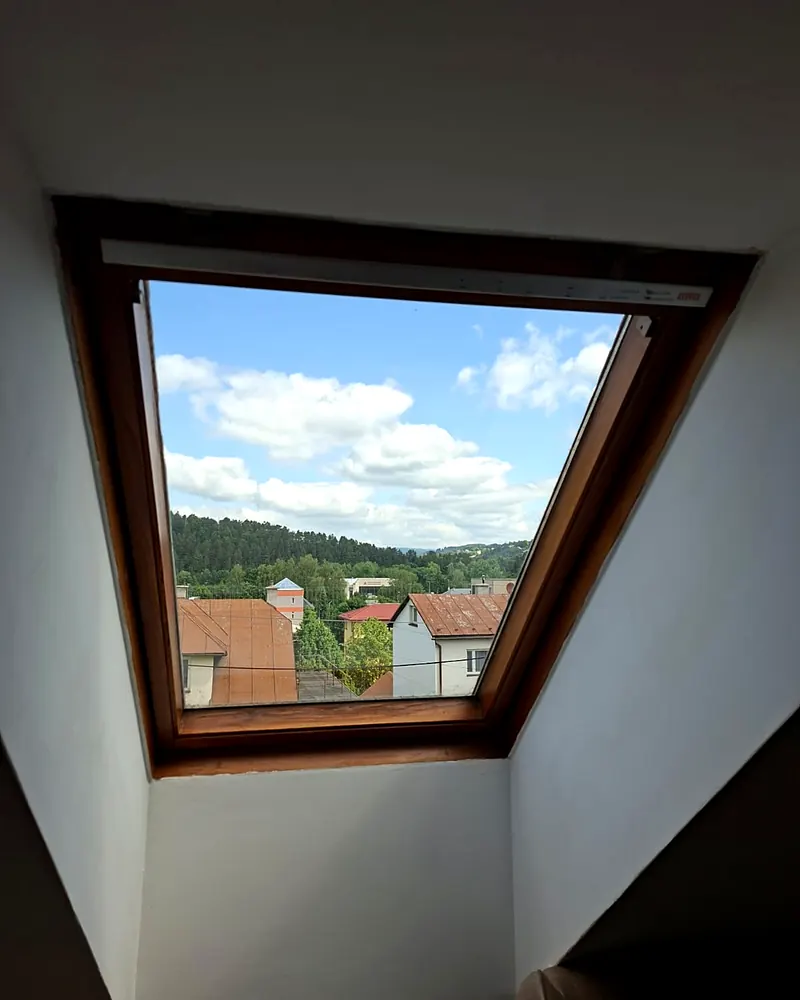 Strešné okno s dreveným rámom a výhľadom na obec a les